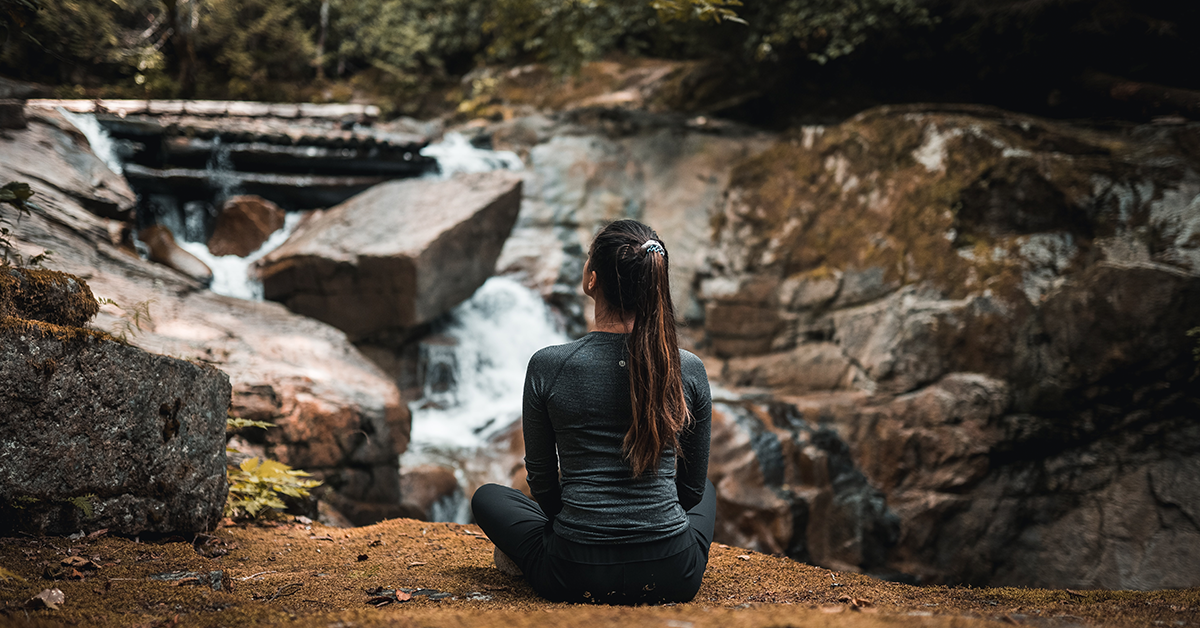A woman practicing yoga by a waterfall. She is using yoga to calm her anxiety