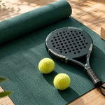 Padel racket and balls beside a green yoga mat and cork blocks.