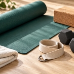 Dumbbells, yoga strap and cork block beside a green yoga mat.